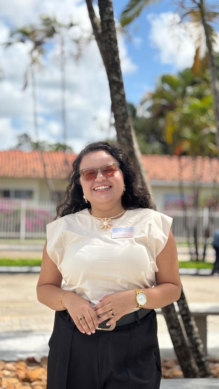 Jailma Silva sorrindo ao ar livre, com óculos, blusa clara e calça preta